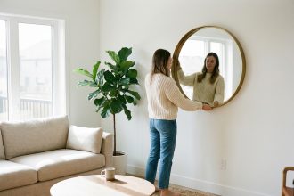 Femme ajustant un grand miroir dans un salon moderne